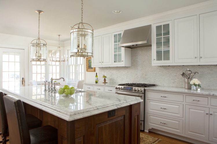 white kitchen cabinets with white marbled backsplash and marble countertops with gold island pendants and stainless steel