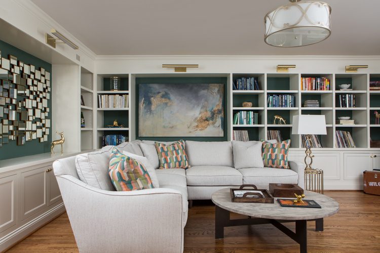 white sectional sofa with white walls and built-in bookcases with green backs of bookcases and coral accents with gold art lighting