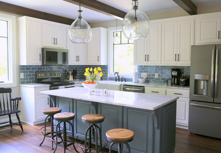 modern farmhouse white kitchen cabinets with dark blue island and blue subway tile and cambria brittanica countertops and industrial bar stools