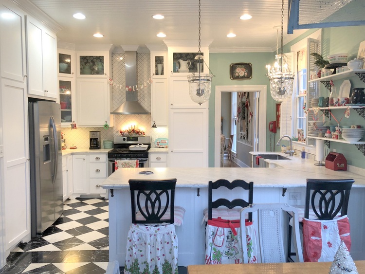 turquoise kitchen with marble countertops and marble floors and mismatched counter stools with vintage aprons