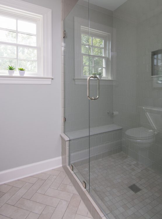 herringbone tile pattern and frameless glass shower door in bathroom by The Decorologist